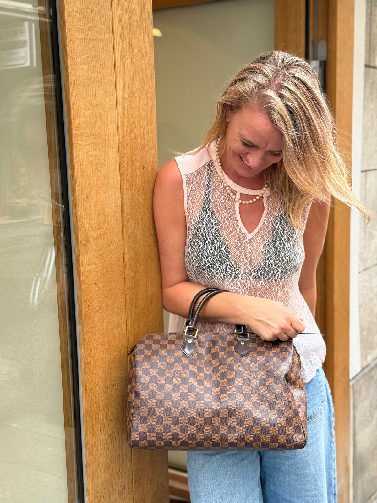 Frau hält eine braune karierte Designerhandtasche vor einer Holztür in der Hand