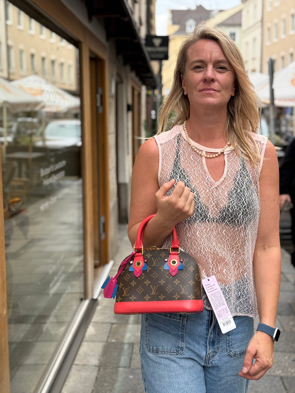 Frau hält eine Louis Vuitton Handtasche mit Monogramm vor einer Boutique in München