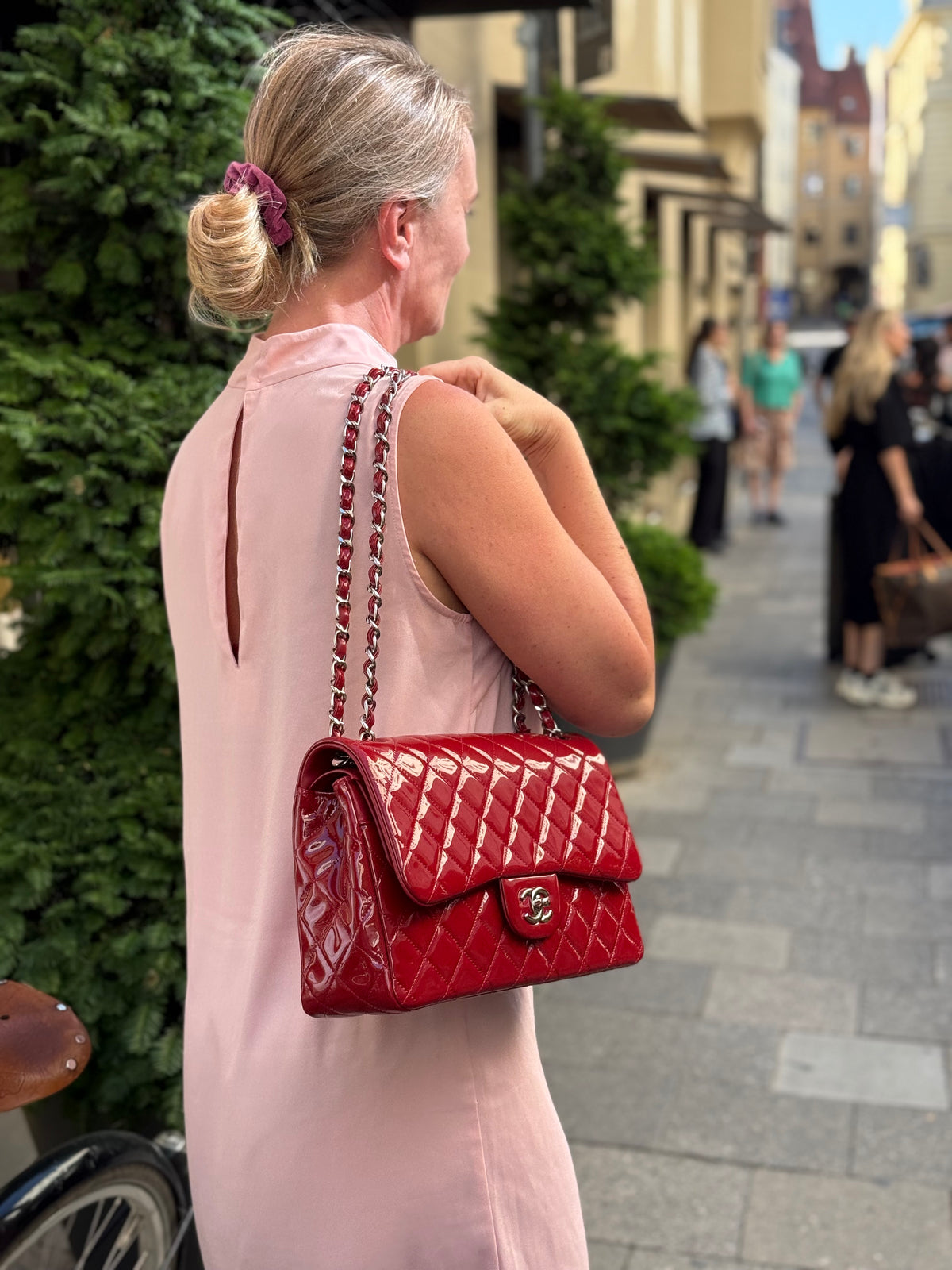 Frau in rosa Kleid trägt eine rote gesteppte Handtasche mit Kettenriemen in einer belebten Straße.
