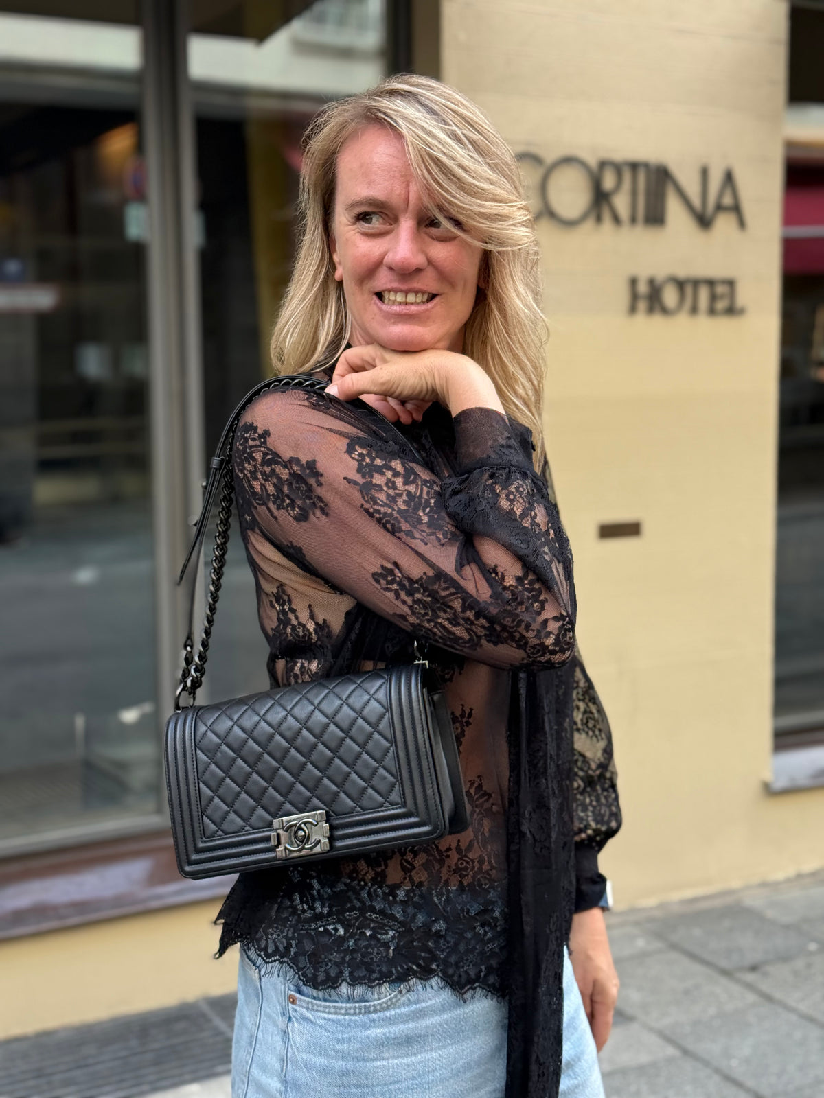Frau mit schwarzer gesteppter Designerhandtasche vor einem Hotelgebäude in München