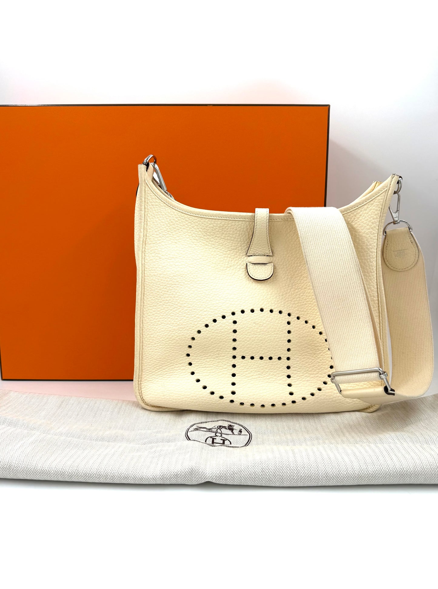 HERMÈS Evelyne 29 Nata Clemence PHW in cremeweiß mit verstellbarem Schulterriemen vor orangefarbenem Hintergrund