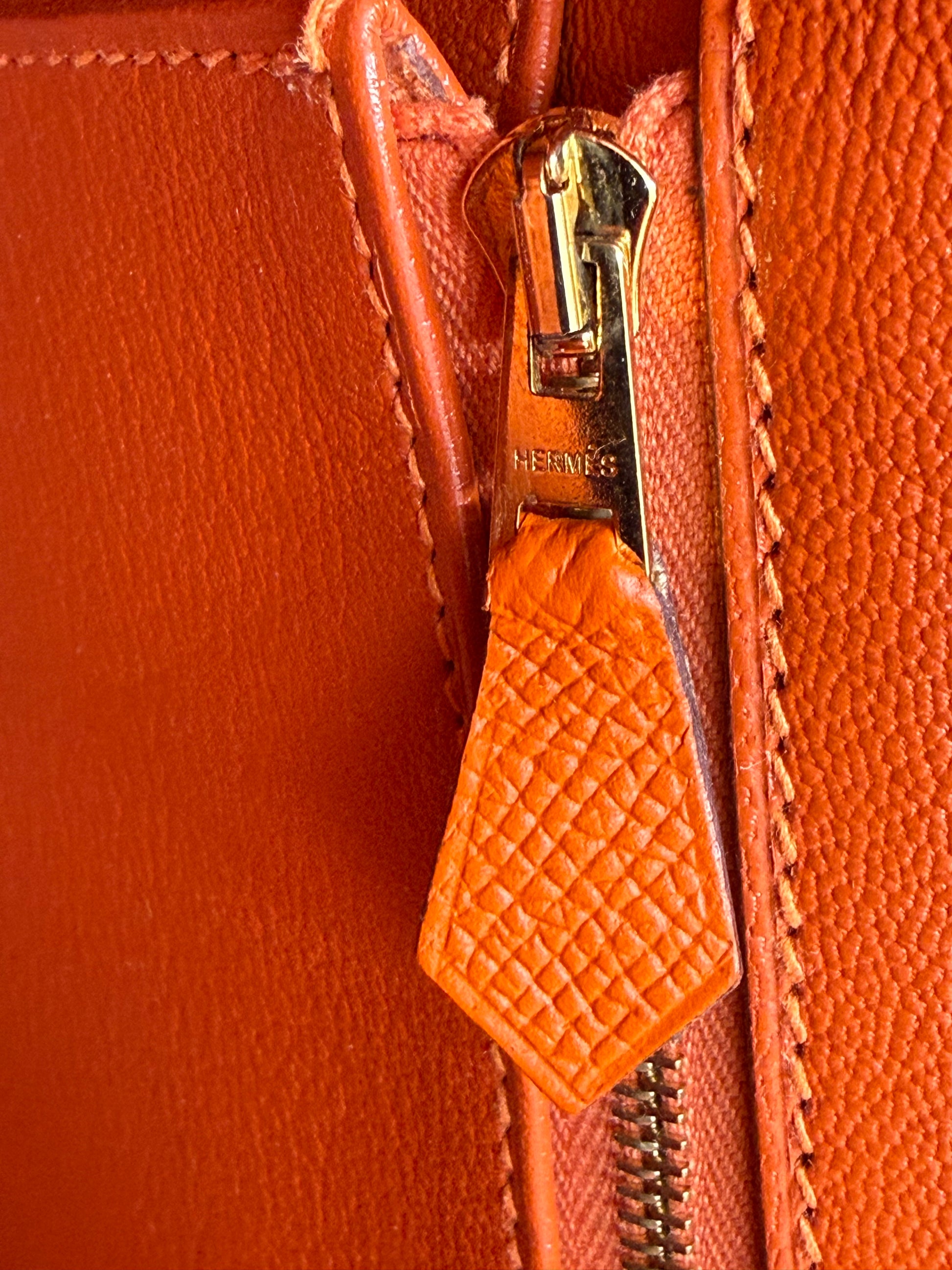 Nahaufnahme des Reißverschlussanhängers der HERMÈS Birkin 35 Epsom orange GHW in Galerieposition 15, Portraitformat.